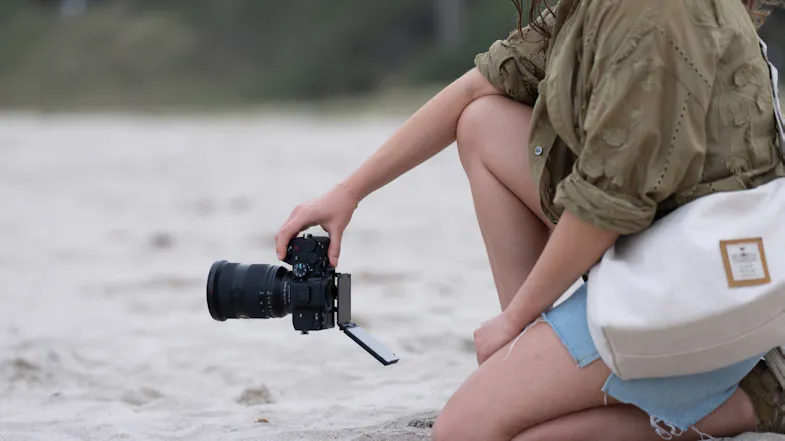 Woman kneeling on the sand, holding the Sony Camera with the screen flipped out Woman kneeling on the sand, holding the Sony Camera with the screen flipped out