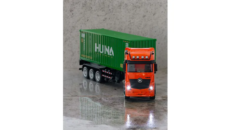 Front view of orange RC container truck with green Huina trailer placed on a tiled surface Front view of orange RC container truck with green Huina trailer placed on a tiled surface