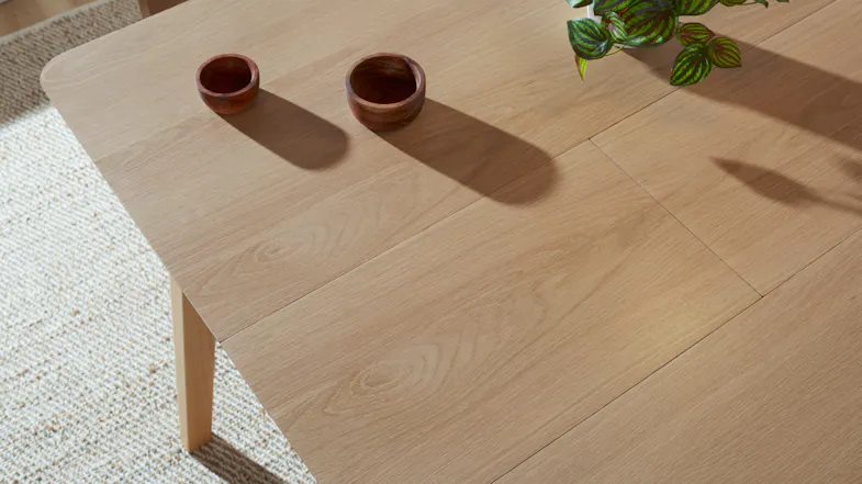 Fully extended wooden dining table with bowls and a plant, showing seamless integration of the extension leaf Fully extended wooden dining table with bowls and a plant, showing seamless integration of the extension leaf