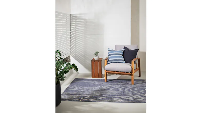 Full outdoor scene with Rivers Rug placed beneath a wooden chair and side table, complemented by a green plant Full outdoor scene with Rivers Rug placed beneath a wooden chair and side table, complemented by a green plant