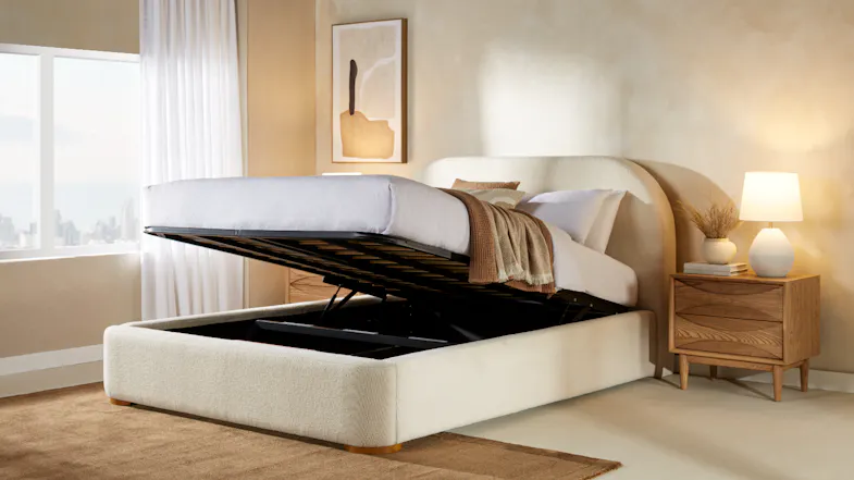 An upholstered queen bed with gas lift storage open, white bedding, a wooden nightstand, and modern decor An upholstered queen bed with gas lift storage open, white bedding, a wooden nightstand, and modern decor