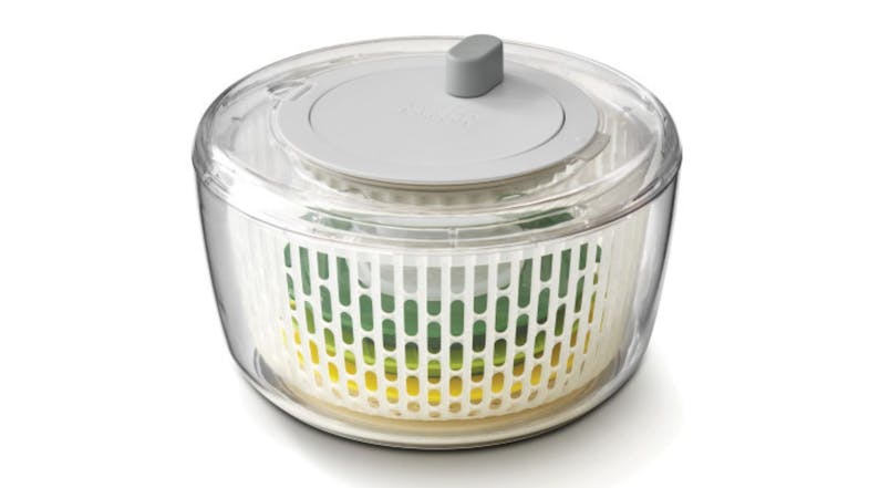 A clear salad spinner with a grey lid and an inner white basket A clear salad spinner with a grey lid and an inner white basket