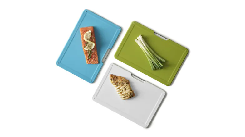 Three colour-coded chopping boards with salmon, chicken, and green onions on textured surfaces Three colour-coded chopping boards with salmon, chicken, and green onions on textured surfaces
