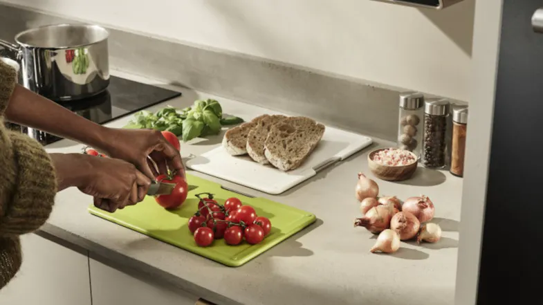 A person slicing tomatoes on a green Joseph Joseph chopping board with under-shelf board storage visible A person slicing tomatoes on a green Joseph Joseph chopping board with under-shelf board storage visible