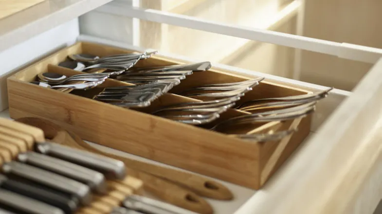 Space-saving bamboo cutlery tray in a drawer holding organised forks and spoons near cooking tools Space-saving bamboo cutlery tray in a drawer holding organised forks and spoons near cooking tools