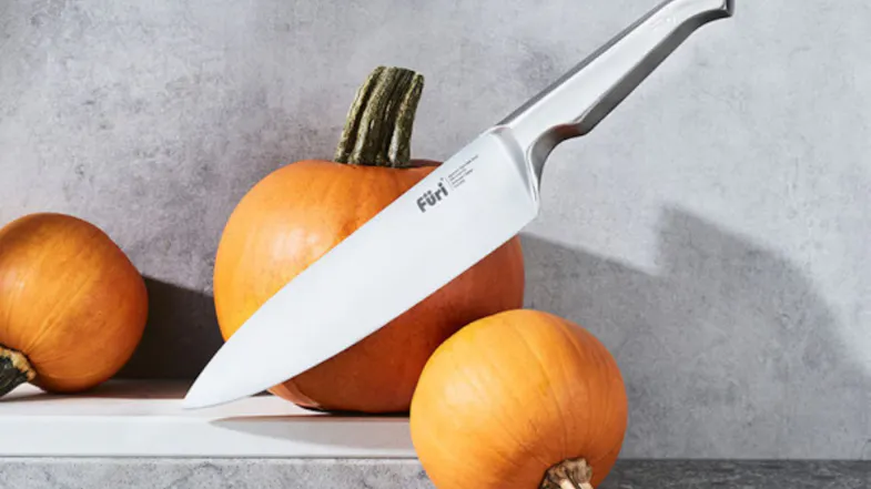 Angled view of a stainless-steel chef knife resting on pumpkins Angled view of a stainless-steel chef knife resting on pumpkins