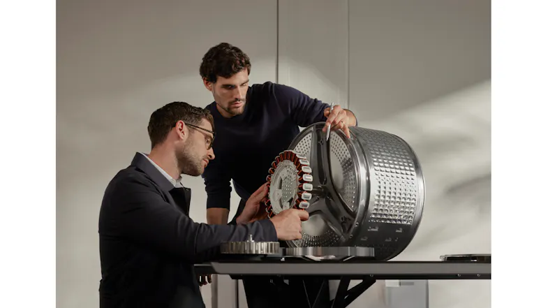 Two people holding a copper-coiled motor attached to a metal drum Two people holding a copper-coiled motor attached to a metal drum