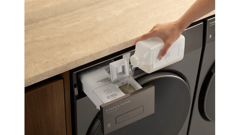 A hand pours liquid from a white bottle into a washer detergent drawer A hand pours liquid from a white bottle into a washer detergent drawer