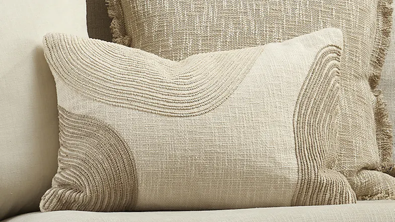 Close-up of ivory cushion featuring raised beige curved line patterns, resting against a textured pillow Close-up of ivory cushion featuring raised beige curved line patterns, resting against a textured pillow