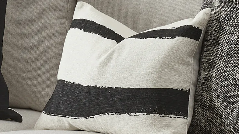 Close-up of an ivory cushion featuring two thick, textured black horizontal stripes on a sofa Close-up of an ivory cushion featuring two thick, textured black horizontal stripes on a sofa