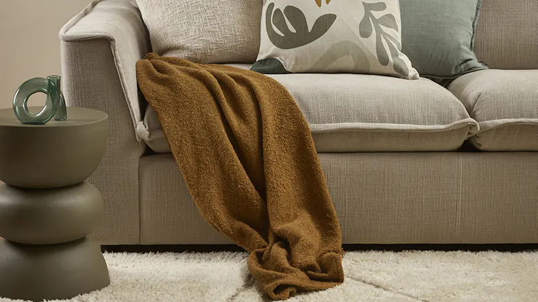 A Lily Throw in Toffee cascading off a light grey sofa onto a plush white shag rug A Lily Throw in Toffee cascading off a light grey sofa onto a plush white shag rug