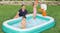 Family enjoying a teal inflatable pool while children play with an orange basketball near the hoop Family enjoying a teal inflatable pool while children play with an orange basketball near the hoop