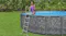 A person climbing on a grey above‑ground pool ladder attached to an outdoor pool in a grassy yard A person climbing on a grey above‑ground pool ladder attached to an outdoor pool in a grassy yard