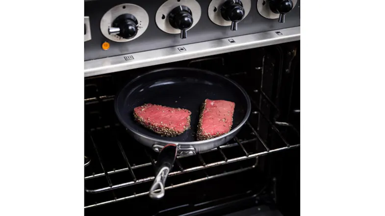 he frying pan sits inside an oven, holding two pieces of seasoned meat he frying pan sits inside an oven, holding two pieces of seasoned meat