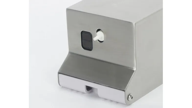 A stainless-steel wall-mounted soap dispenser is shown at an angle with floating green leaves A stainless-steel wall-mounted soap dispenser is shown at an angle with floating green leaves