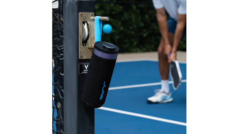 JLab Go Party speaker hanging by its blue strap from a metal post on a pickleball court JLab Go Party speaker hanging by its blue strap from a metal post on a pickleball court