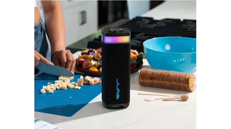 JLab JBuds Party speaker on a kitchen counter near a charcuterie board and blue bowl JLab JBuds Party speaker on a kitchen counter near a charcuterie board and blue bowl