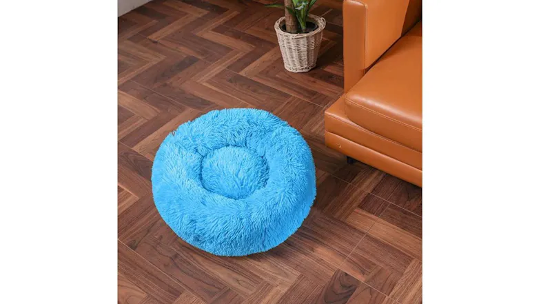 A blue Hod Snuggly Pooch Dog Bed is placed on a wooden floor beside a brown leather sofa and a small potted plant A blue Hod Snuggly Pooch Dog Bed is placed on a wooden floor beside a brown leather sofa and a small potted plant