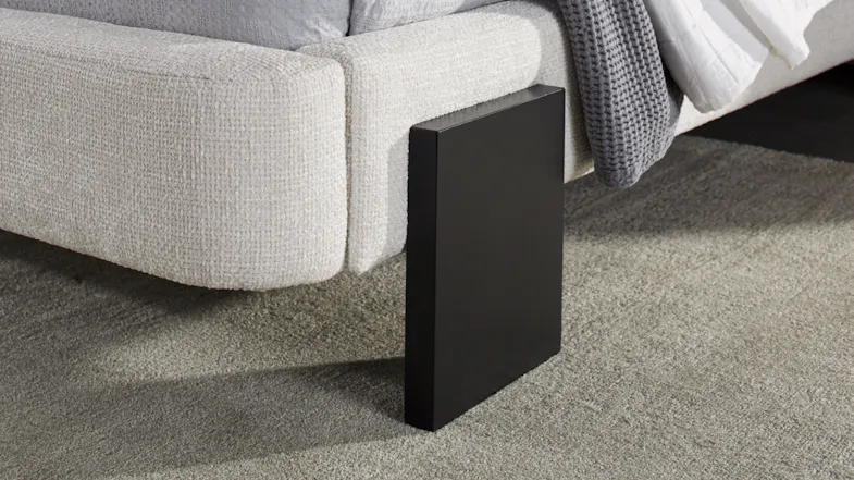 Close-up view of a minimalist black rectangular leg on a tan rug Close-up view of a minimalist black rectangular leg on a tan rug
