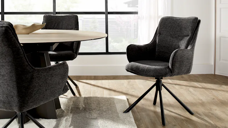 A charcoal upholstered bar stool positioned beside a round dining table in a bright room A charcoal upholstered bar stool positioned beside a round dining table in a bright room