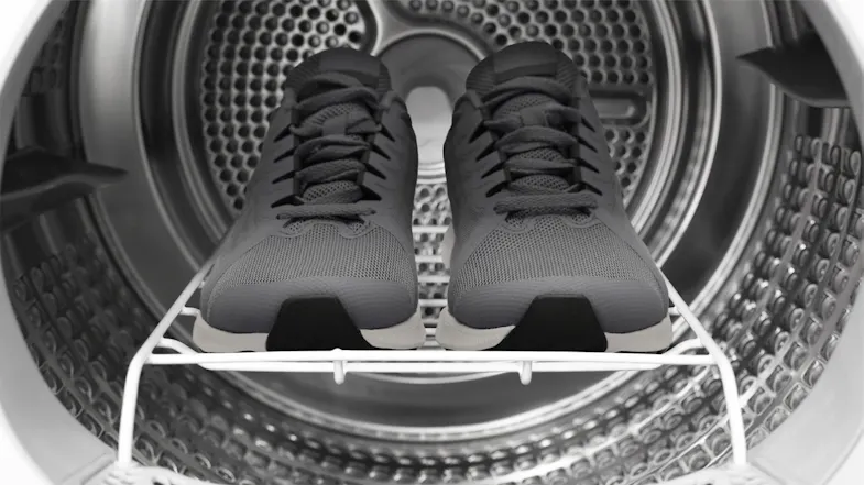 Close-up view of grey sneakers resting on a drying rack inside a dryer drum Close-up view of grey sneakers resting on a drying rack inside a dryer drum