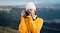 Frontal view of a woman in a beanie photographing a mountain range Frontal view of a woman in a beanie photographing a mountain range