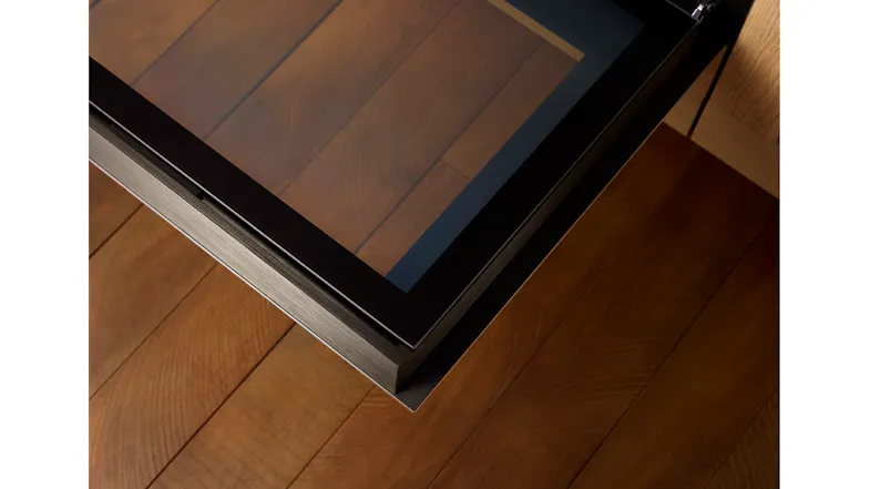 Close‑up of the oven door’s glass edge and brushed metal trim positioned above wooden flooring Close‑up of the oven door’s glass edge and brushed metal trim positioned above wooden flooring