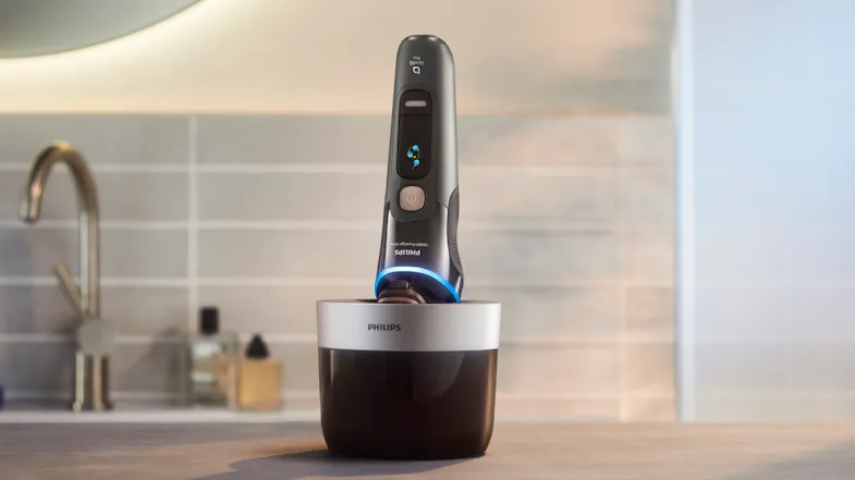 Philips cordless shaver resting vertically in a black and silver cleaning pod Philips cordless shaver resting vertically in a black and silver cleaning pod