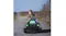 A kid is driving a green ride-on tractor on a rural gravel road lined with leafless trees A kid is driving a green ride-on tractor on a rural gravel road lined with leafless trees