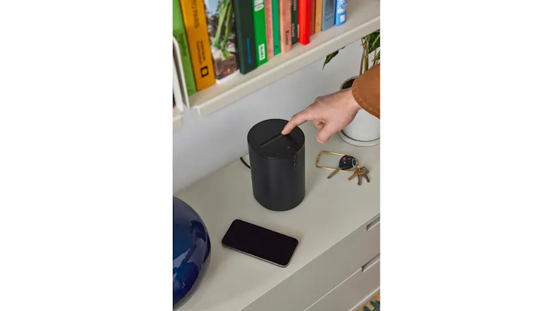 Hand using the top touch controls on an oval speaker Hand using the top touch controls on an oval speaker