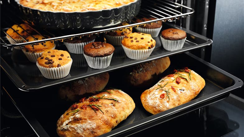 Multiple trays of muffins and bread are baking in an oven Multiple trays of muffins and bread are baking in an oven