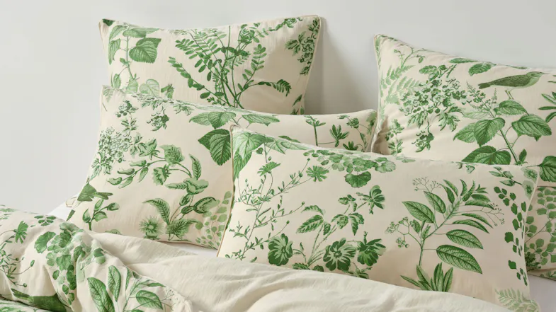 Close-up of several pillows from the Lindy Natural set, showing the cream fabric covered in green botanical prints Close-up of several pillows from the Lindy Natural set, showing the cream fabric covered in green botanical prints