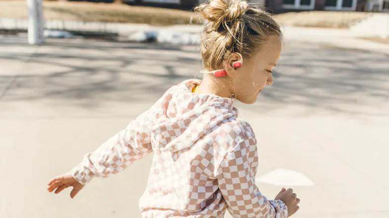 Side profile of a girl wearing JBL open-ear headphones outdoors Side profile of a girl wearing JBL open-ear headphones outdoors