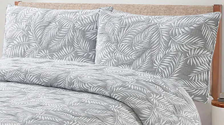 Close‑up of the bed pillows and coverlet, highlighting the quilted texture and fern leaf design in silver and white Close‑up of the bed pillows and coverlet, highlighting the quilted texture and fern leaf design in silver and white