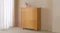 Jasper 5 Drawer Tallboy in light oak finish, standing against a beige wall Jasper 5 Drawer Tallboy in light oak finish, standing against a beige wall