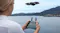 A woman uses a screen controller to fly a drone over a blue lake A woman uses a screen controller to fly a drone over a blue lake