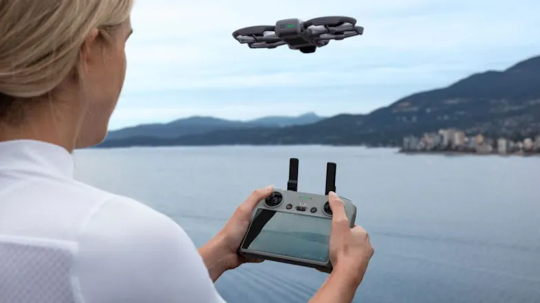 A woman uses a screen controller to fly a drone over a blue lake A woman uses a screen controller to fly a drone over a blue lake