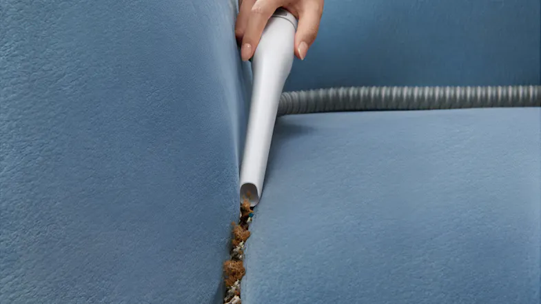 A slim crevice tool reaching between the sofa to remove debris A slim crevice tool reaching between the sofa to remove debris