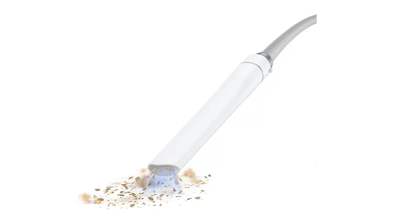 A white vacuum nozzle is suctioning up various small seeds and debris A white vacuum nozzle is suctioning up various small seeds and debris