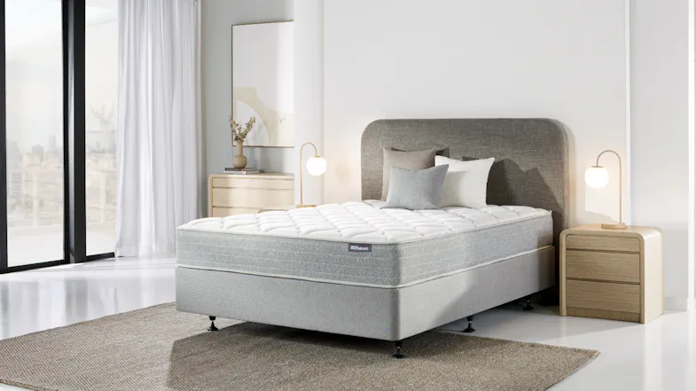ull view of a Sealy Posture Life Comfort mattress and base set on a rug in a bright room ull view of a Sealy Posture Life Comfort mattress and base set on a rug in a bright room