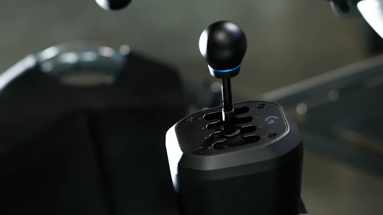 Lifestyle image of the Logitech G RS H Shifter mounted beside a racing seat, with the gear lever upright Lifestyle image of the Logitech G RS H Shifter mounted beside a racing seat, with the gear lever upright