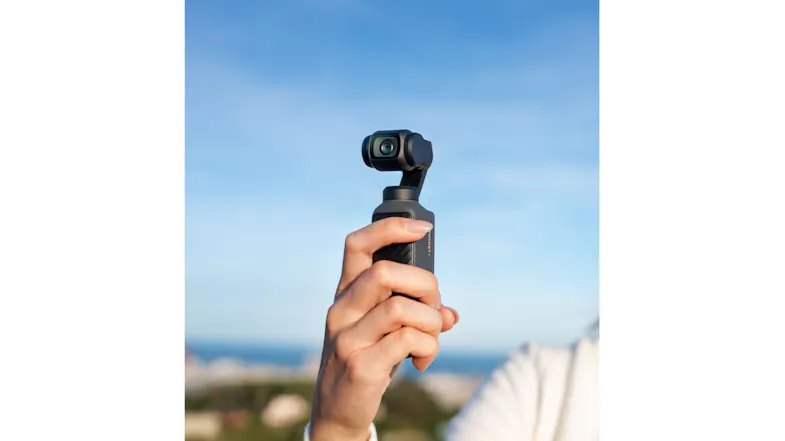 Hand holding the compact DJI device against a blurred sky background Hand holding the compact DJI device against a blurred sky background