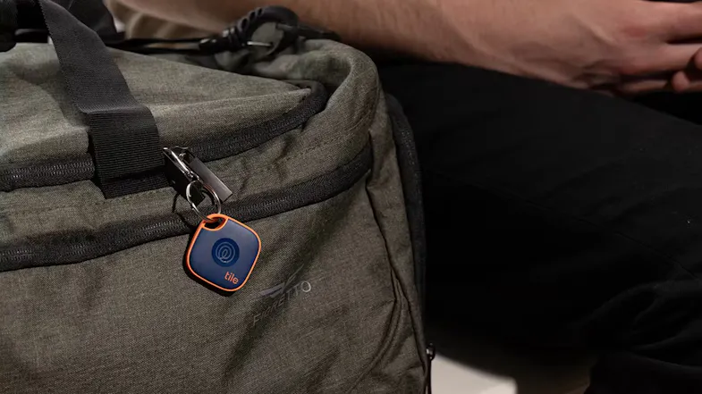 The Tile tracker clipped to the zipper of an olive green duffel bag The Tile tracker clipped to the zipper of an olive green duffel bag
