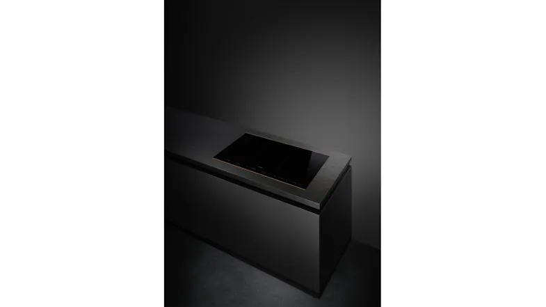 Angled perspective of the black Smeg 6‑zone induction cooktop installed flush into a dark stone kitchen island Angled perspective of the black Smeg 6‑zone induction cooktop installed flush into a dark stone kitchen island