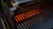 Close‑up inside the BBQ showing stainless steel cooking grates with glowing heat bars beneath Close‑up inside the BBQ showing stainless steel cooking grates with glowing heat bars beneath
