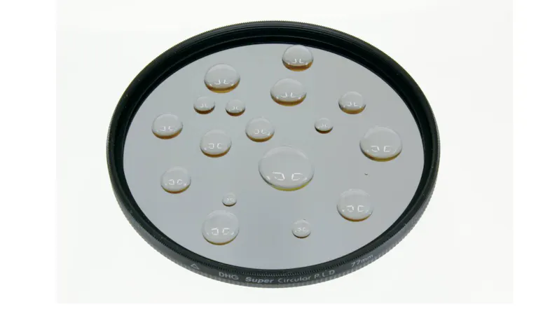 Circular glass filter with large water droplets beading on the surface Circular glass filter with large water droplets beading on the surface