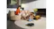 A robotic vacuum cleans a light-coloured rug in a modern living room while people sit on a sofa nearby A robotic vacuum cleans a light-coloured rug in a modern living room while people sit on a sofa nearby