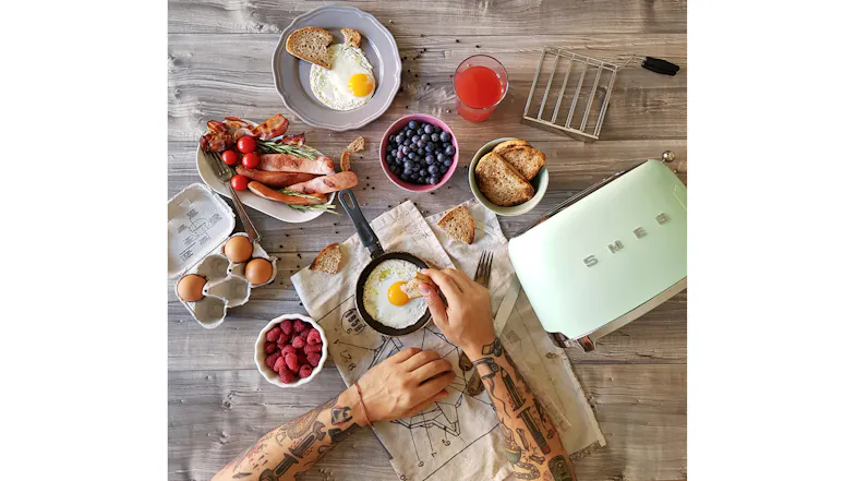 Overhead lifestyle scene featuring the pastel green Smeg toaster alongside breakfast foods Overhead lifestyle scene featuring the pastel green Smeg toaster alongside breakfast foods