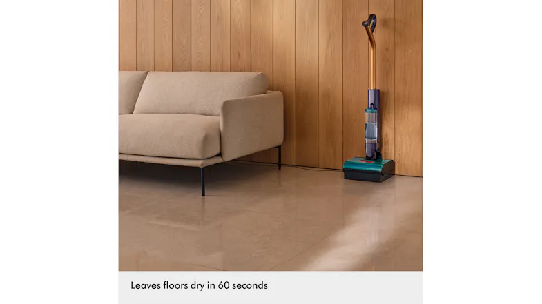 The Dyson Clean+Wash Hygiene cleaner docked upright beside a sofa on a smooth hard floor The Dyson Clean+Wash Hygiene cleaner docked upright beside a sofa on a smooth hard floor