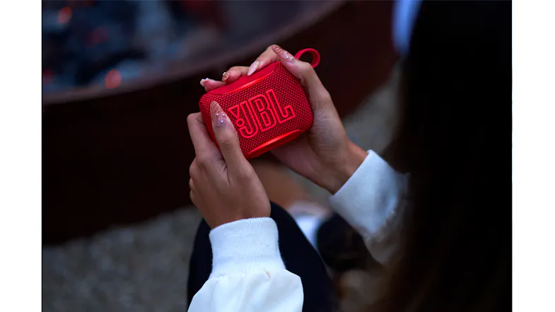 Close-up view of hands holding a red speaker with raised logo texture Close-up view of hands holding a red speaker with raised logo texture